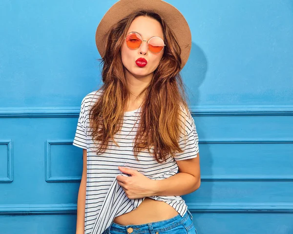 スタイリッシュな少女モデルではカジュアルな夏服と赤い唇 青い壁に近いポーズで茶色の帽子 空気のキスを与える — ストック写真