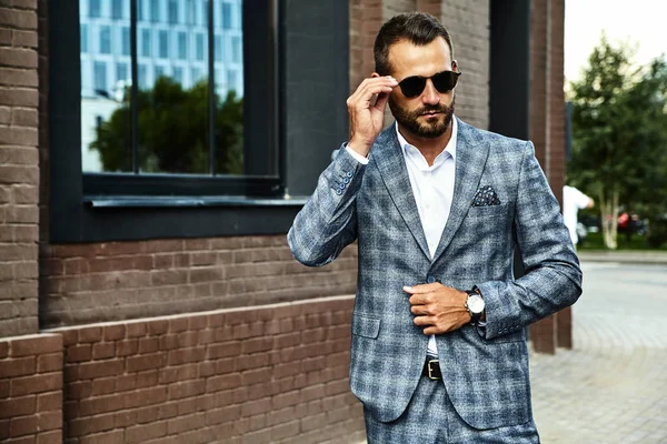 Portrait of sexy handsome fashion businessman model dressed in elegant checkered suit posing on street background. Metrosexual