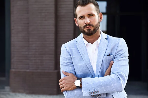 Portrait of sexy handsome fashion businessman model dressed in elegant blue suit posing on street background. Metrosexual