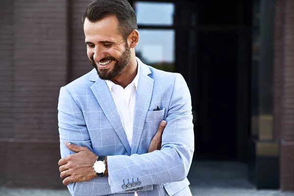 Portrait of sexy handsome fashion businessman model dressed in elegant blue suit posing on street background. Metrosexual