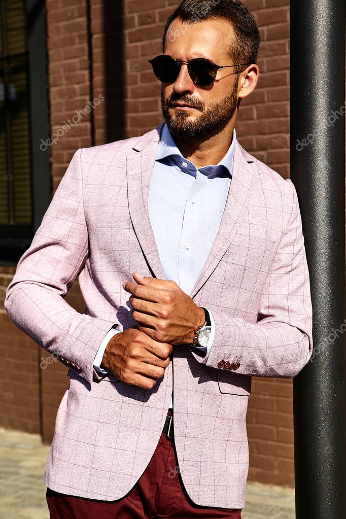 Portrait of sexy handsome fashion businessman model dressed in elegant suit posing near brick wall on the street background. Metrosexual