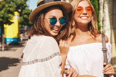 İki genç şık hippi esmer ve sarışın Bayan modelleri yaz güneşli günde sokak arka plan üzerinde poz beyaz hipster giysileri moda portre. Hiç makyaj