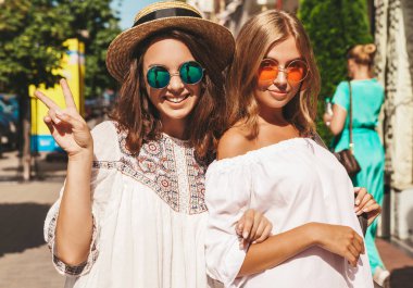 İki genç şık hippi esmer ve sarışın Bayan modelleri yaz güneşli günde sokak arka plan üzerinde poz beyaz hipster giysileri moda portre. Hiç makyaj