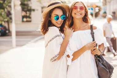 İki genç şık hippi esmer ve sarışın Bayan modelleri yaz güneşli günde sokak arka plan üzerinde poz beyaz hipster giysileri moda portre. Delirmek
