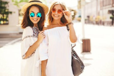 İki genç şık hippi esmer ve sarışın Bayan modelleri yaz güneşli günde sokak arka plan üzerinde poz beyaz hipster giysileri moda portre. Delirmek