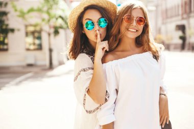 İki genç şık hippi esmer ve sarışın kadın yaz hipster moda portre elbise sokak arka plan üzerinde poz. Modelleri sırlarını, dedikodu paylaşır. Parmak ağız yakınındaki