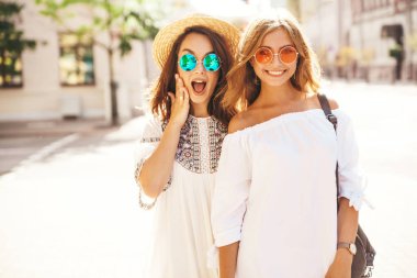 İki genç şık hippi esmer ve sarışın Bayan modelleri moda portre. Arkadaşlarım Beyaz yaz hipster içinde poz sokak arka plan üzerinde elbise. Sürpriz yüz, duygular