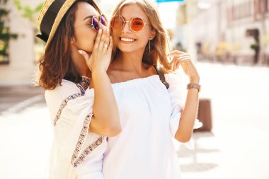İki genç şık hippi esmer ve sarışın kadın sokak arka plan üzerinde poz beyaz hipster giyim yaz güneşli bir günde moda portre. Sırlar, dedikodu paylaşmak modelleri.