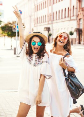 İki genç şık hippi esmer ve sarışın Bayan modelleri yaz güneşli günde sokak arka plan üzerinde poz beyaz hipster giysileri moda portre. Delirmek
