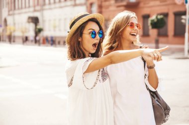 İki genç şık hippi esmer ve sarışın Bayan modelleri yaz güneşli günde sokak arka plan üzerinde poz beyaz hipster giysileri moda portre. Dükkanı satış işaret
