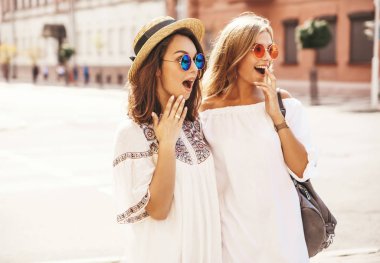 İki genç şık hippi esmer ve sarışın Bayan modelleri moda portre. Arkadaşlarım Beyaz yaz hipster içinde poz sokak arka plan üzerinde elbise. Sürpriz yüz, duygular