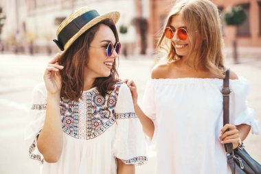 İki genç şık hippi esmer ve sarışın Bayan modelleri yaz güneşli günde sokak arka plan üzerinde poz beyaz hipster giysileri moda portre. Delirmek
