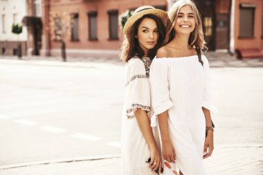 İki genç şık hippi esmer ve sarışın Bayan modelleri yaz güneşli günde sokak arka plan üzerinde poz beyaz hipster giysileri moda portre. Hiç makyaj