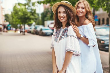 İki genç şık hippi esmer ve sarışın Bayan modelleri yaz güneşli günde sokak arka plan üzerinde poz beyaz hipster giysileri moda portre. Hiç makyaj