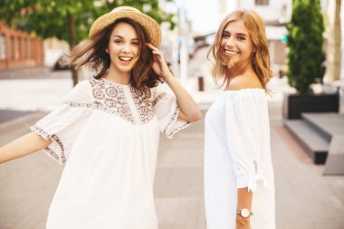 İki genç şık hippi esmer ve sarışın Bayan modelleri sokak arka plan üzerinde poz beyaz hipster giyim yaz güneşli bir günde makyaj olmadan moda portre. Dön
