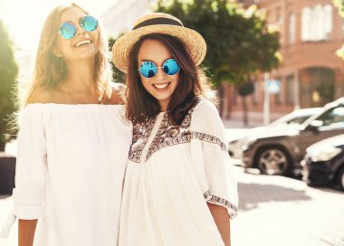 İki genç şık hippi esmer ve sarışın Bayan modelleri yaz güneşli günde sokak arka plan üzerinde poz beyaz hipster giysileri moda portre. Delirmek