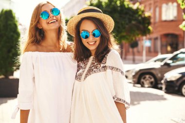 İki genç şık hippi esmer ve sarışın Bayan modelleri yaz güneşli günde sokak arka plan üzerinde poz beyaz hipster giysileri moda portre. Delirmek