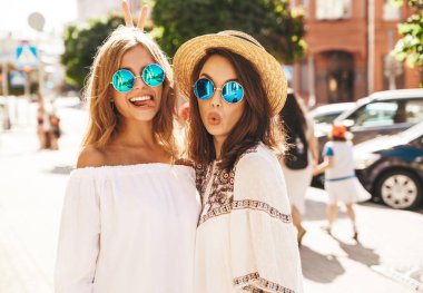 İki genç şık hippi esmer ve sarışın Bayan modelleri sokak arka plan üzerinde poz beyaz hipster giyim yaz güneşli bir günde makyaj olmadan moda portre. Delirmek
