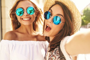 İki genç kadın gülümseyen hippi esmer ve sarışın kadın modeli selfie sosyal medya için Smartphone cep telefonu ile sokak arka plan üzerinde çekim beyaz hippi elbise yaz. Sürpriz yüz, duygular,