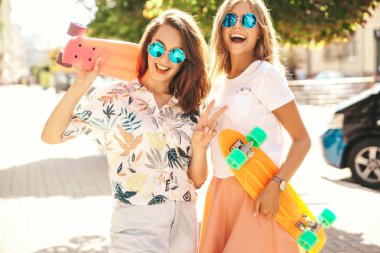 İki genç şık gülümseyen hippi esmer ve sarışın Bayan modelleri yaz hipster giysileri sokak arka plan üzerinde poz kuruş kaykay ile. Sürpriz yüz, duygular