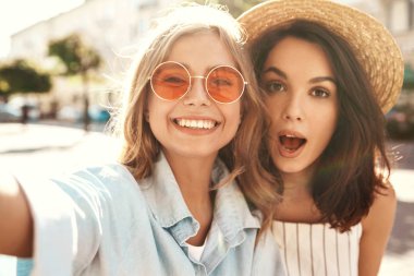 İki genç kadın şık hippi esmer ve sarışın Bayan modelleri yaz güneşli günde selfie sosyal medya için Smartphone cep telefonu ile sokak arka plan üzerinde çekim hipster giysili