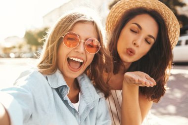İki genç kadın şık hippi esmer ve sarışın Bayan modelleri yaz güneşli günde selfie sosyal medya için Smartphone cep telefonu ile sokak arka plan üzerinde çekim hipster giysili. Hava öpücük vererek