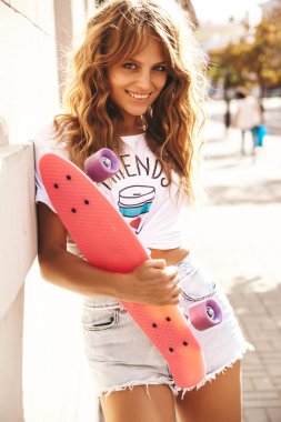 Güzel şirin sarışın genç model makyaj yaz hipster beyaz giysileri olmadan sokak arka plan üzerinde poz pembe kuruş kaykay ile