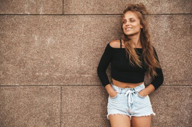 Güzel sevimli gülümseyen sarışın genç model yaz hipster rahat giysileri sokak duvarının yakınında poz