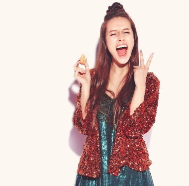 Güzel beyaz gülümseyen hipster esmer kadın modelinde parlak parlak yaz şık ceket ve yeşil elbise beyaz arka plan üzerinde izole yansıtan. Fransız acıbadem kurabiyesi yeme ve barış işareti gösterilen