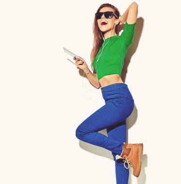 Beyaz smartphone kulaklık ile müzik dinleme güneş gözlüklü esmer kadın kız rahat yeşil hipster yaz giysileri hiç makyaj ile gülümseyen güzel deli portresi izole