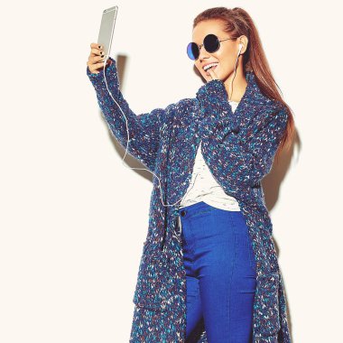 güzel mutlu sevimli gülümseyen esmer kadın kız rahat mavi hipster yaz giysileri beyaz smartphone kulaklık ile müzik dinleyip selfie güneş gözlüğü izole hiç makyaj ile portresi