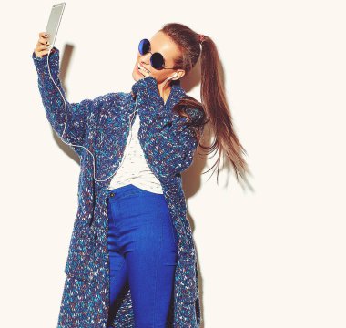 güzel mutlu sevimli gülümseyen esmer kadın kız rahat mavi hipster yaz giysileri beyaz smartphone kulaklık ile müzik dinleyip selfie güneş gözlüğü izole hiç makyaj ile portresi