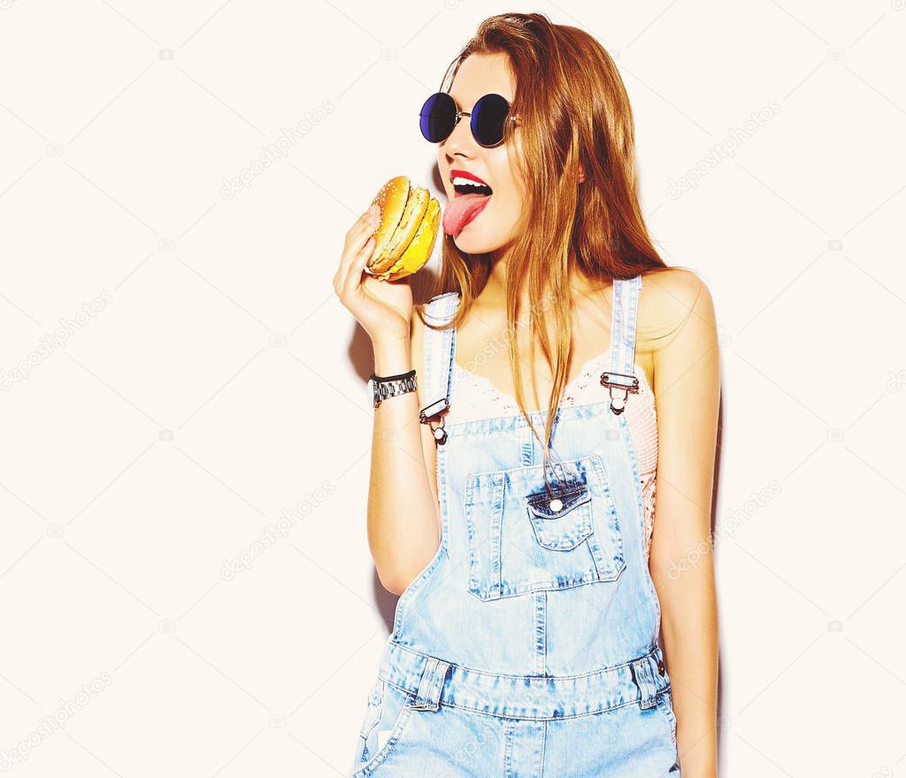 Funny crazy glamor stylish sexy smiling beautiful young blond woman model in summer bright hipster jeans clothes eating hamburger