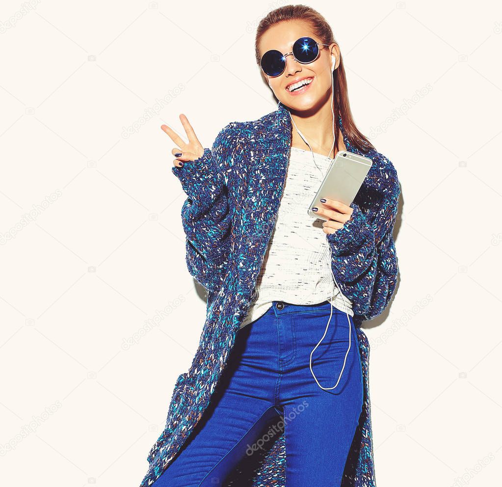 portrait of beautiful happy cute smiling brunette woman girl in casual blue hipster summer clothes with no makeup isolated on white in sunglasses listening music in smartphone with headphones showing peace sign