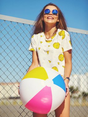 Komik deli sihir şık gülümseyen güzel genç kadın model parlak hipster yaz rahat giysileri demir ızgara ve mavi arkasındaki sokakta poz gökyüzü. Renkli şişme top kayan ile oynamak