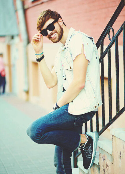 Funny smiling hipster handsome man guy in stylish summer clothes in the street in sunglasses