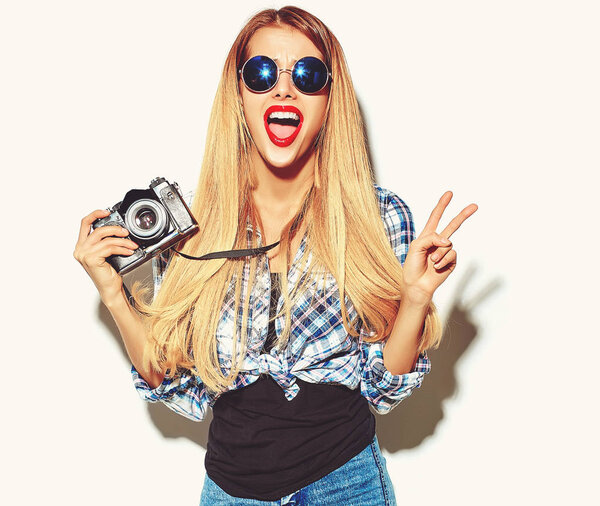beautiful happy cute blond woman girl in casual summer hipster clothes with red lips takes photos holding retro photographic camera showing peace sign