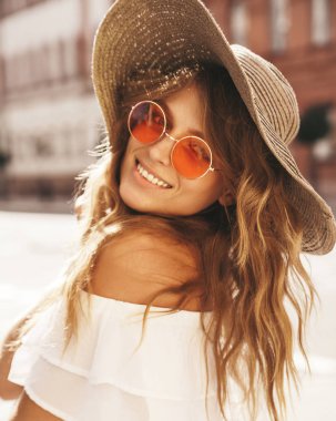 Hiç makyaj yaz hipster beyaz elbise ve sokak arka plan üzerinde poz büyük plaj şapka ile gülümseyen güzel sarışın genç model portresi 