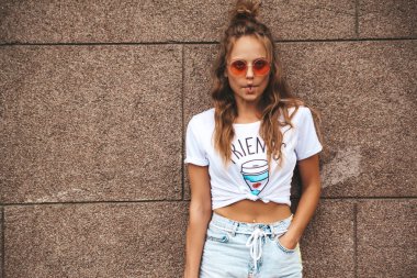 Sokakta duvarının yakınında poz yaz hipster beyaz giysili güzel şirin sarışın genç modeli. Yapma komik balık yüz