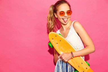 Penny kaykay ile portre sarışın genç şık gülümseyen bir kadın. Studio pembe duvarının yakınında poz yaz beyaz elbiseli kız