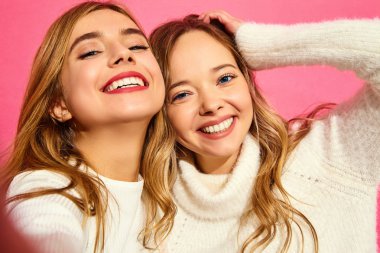 İki genç sarışın kadın gülümseyerek şık portresi. Kızlar yaz hipster elbiseleri giymiş. Olumlu modelleri pembe arka plan Smartphone'da selfie yapma