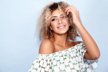 Gülümseyen ve kameraya bakarak sarışın Afrika saç modeli ile mutlu sevimli kadın portresi. Mavi arka plan üzerinde poz trendy yaz giysileri kızı