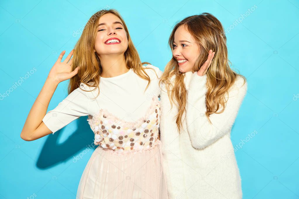 Two young beautiful smiling hipster girls in trendy summer white clothes. Sexy carefree women posing near blue wall. Positive models