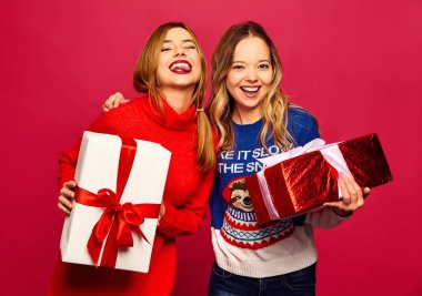 Noel, x-mas, kavram. İki şık kazak güzel kadın gülümsüyor. Kızlar kırmızı zemin üzerine poz. Modelleri ile büyük hediye kutuları. Kutlama için hazır eğleniyor. En iyi arkadaşlarından parlak tatil