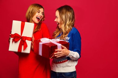 Noel, x-mas, kavram. İki şık kazak güzel kadın gülümsüyor. Kızlar kırmızı zemin üzerine poz. Modelleri ile büyük hediye kutuları. Kutlama için hazır eğleniyor. En iyi arkadaşlarından parlak tatil