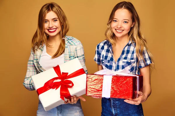 圣诞节 两个穿着时尚服装的微笑的美女 女孩在金色背景上摆姿势 带有大礼品盒的模型 玩得开心 准备庆祝 最好的朋友的明亮假期 — 图库照片