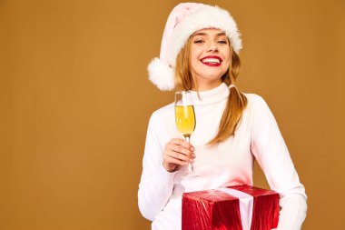 Noel, x-mas, kavram. Beyaz Kış kazaklı gülümseyen güzel kadın. Altın arka plan üzerinde poz kız. Şampanya içmek büyük hediye kutusu ile model. Eğleniyor, kutluyor yeni yıl