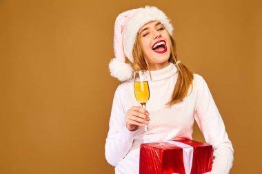 Noel, x-mas, kavram. Beyaz Kış kazaklı gülümseyen güzel kadın. Altın arka plan üzerinde poz kız. Şampanya içmek büyük hediye kutusu ile model. Eğleniyor, kutluyor yeni yıl