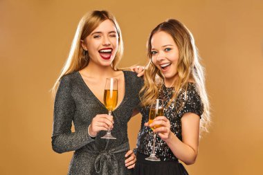 Güzel sarışın kadınlar yeni moda partide eğleniyor Year.Models kutluyor. Mutlu gülümseyen kız şık göz alıcı elbiseler ile şampanya bardağı. Altın arka plan üzerinde izole