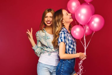 İki kareli gömlek giysili güzel kadın gülümsüyor. Kızlar kırmızı zemin üzerine poz. Pembe balonlu modelleri. Eğleniyor, kutlama Doğum günü veya tatil parti için hazır